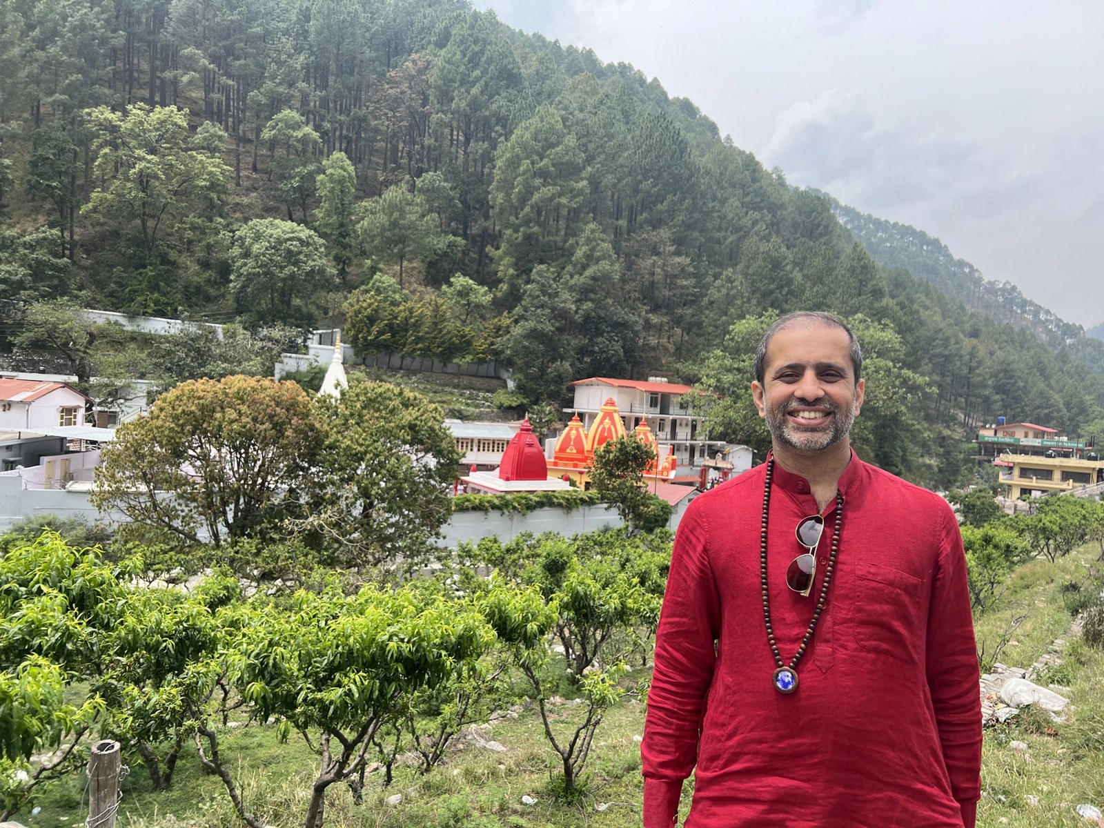 Poorvesh Thakkar above Kainchi Dham, Nainital — the ashram's red rooftops in the valley behind him